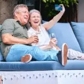 A happy senior expat couple taking a selfie while relaxing on an outdoor sofa with drinks, enjoying retirement in Spain with peace of mind from 247 Expat Insurance.