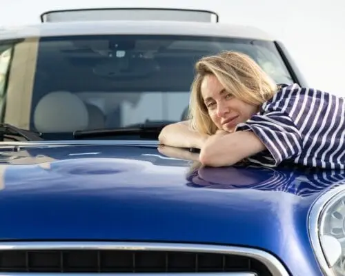 Middle woman driver embracing hood of car after detailing, polishing. Car insurance advertisement