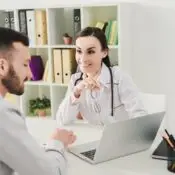 smiling doctor and man discussing health insurance and looking on laptop screen in clinic