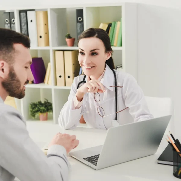 smiling doctor and man discussing health insurance and looking on laptop screen in clinic smiling doctor and man discussing health insurance and looking on laptop screen in clinic